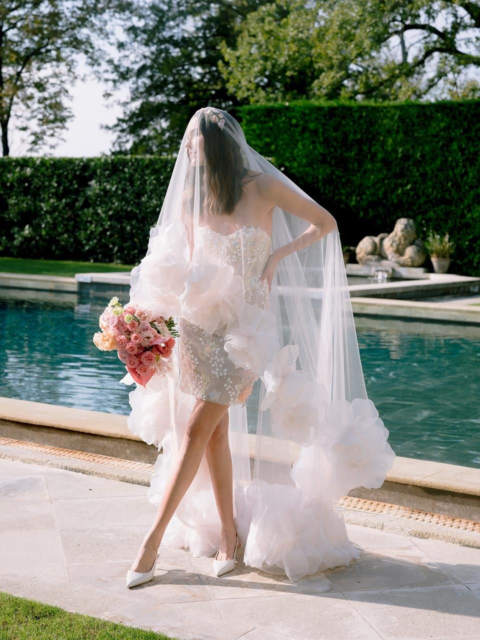 Sposa velata con bouquet rosa a bordo piscina