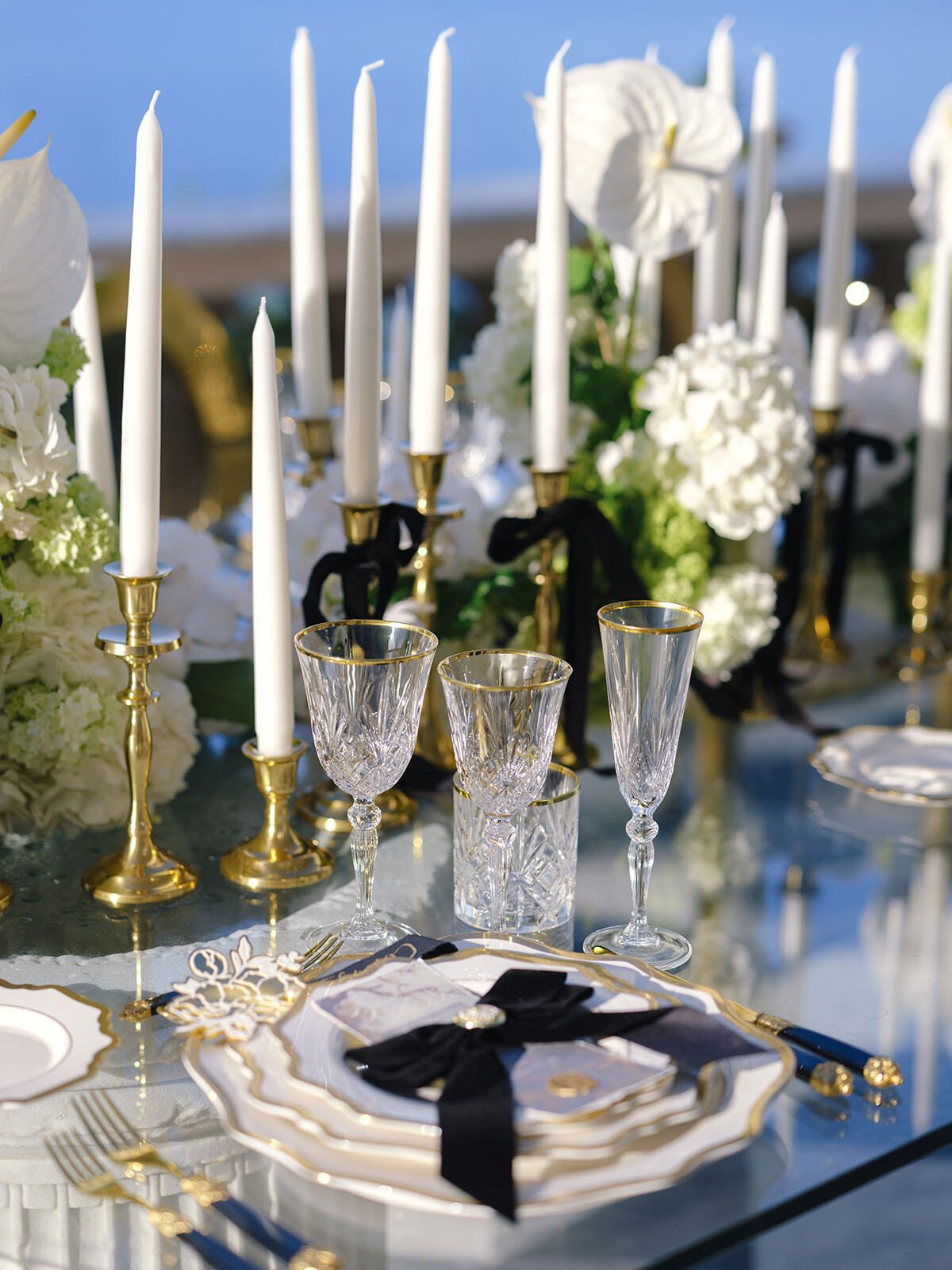 Tafel mit goldenen Kerzenleuchtern, schwarzen Schleifen und weißen Blumen am Meer
