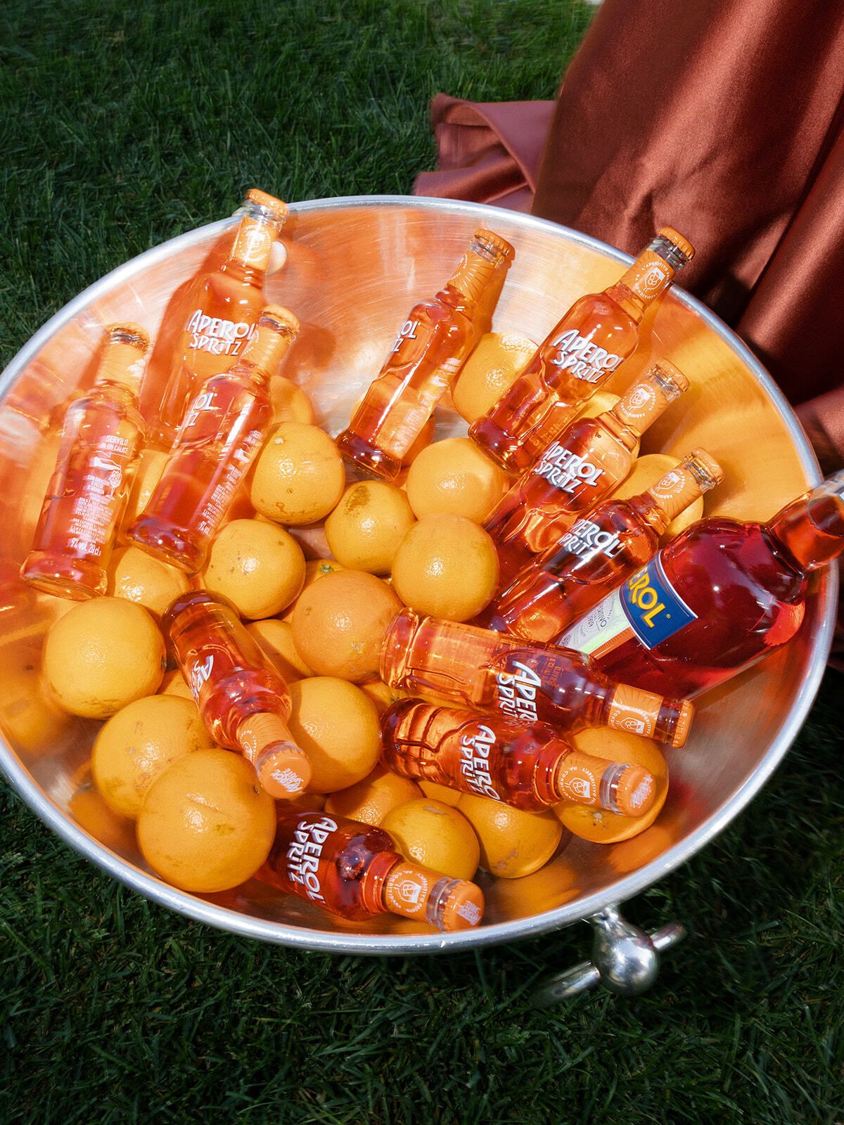 Silberkübel mit Spritz-Flaschen und Orangen auf dem Rasen