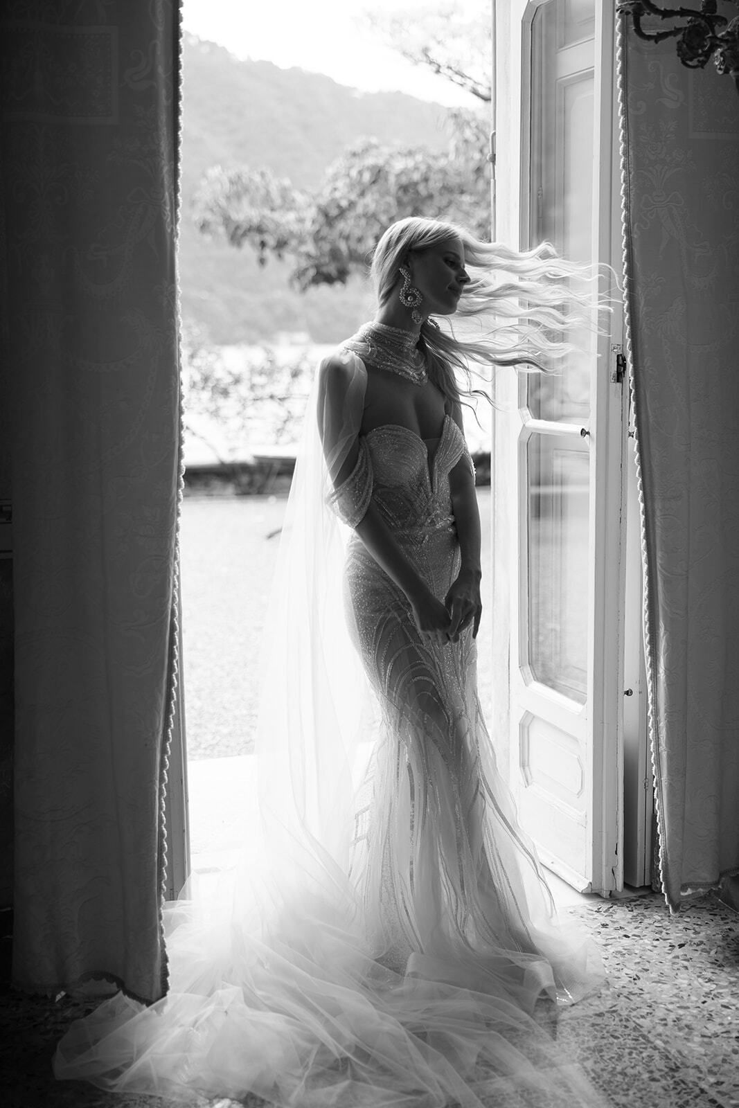 Foto en blanco y negro de una novia en una ventana francesa junto al lago