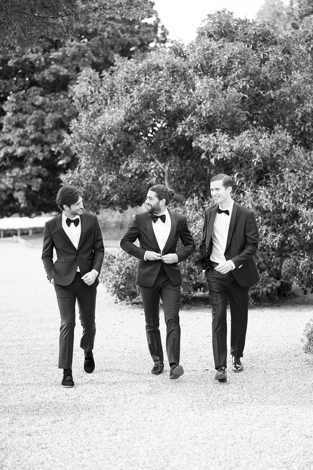 Photo en noir et blanc du marié et de ses garçons d’honneur marchant
