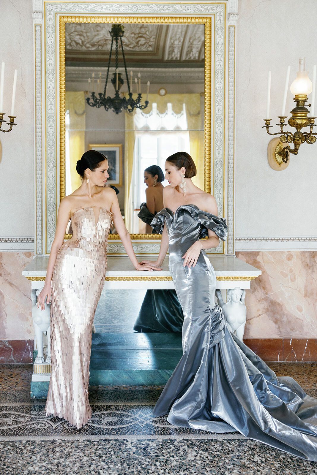 Women in metallic gowns posing in a mirrored villa salon