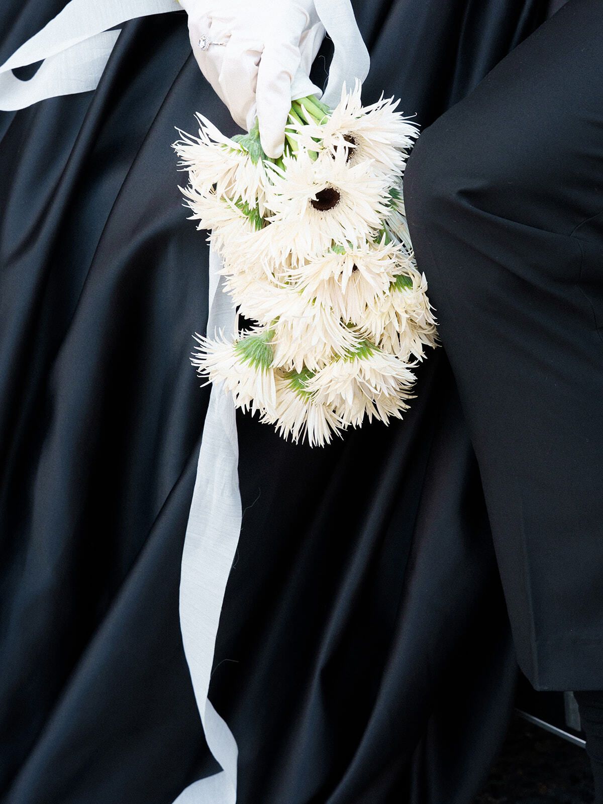 Strauß weißer Gerbera vor einem schwarzen Kleid