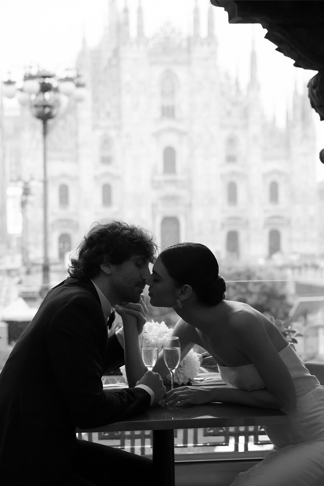 Foto en blanco y negro de una pareja besándose en un café frente a la catedral de Milán