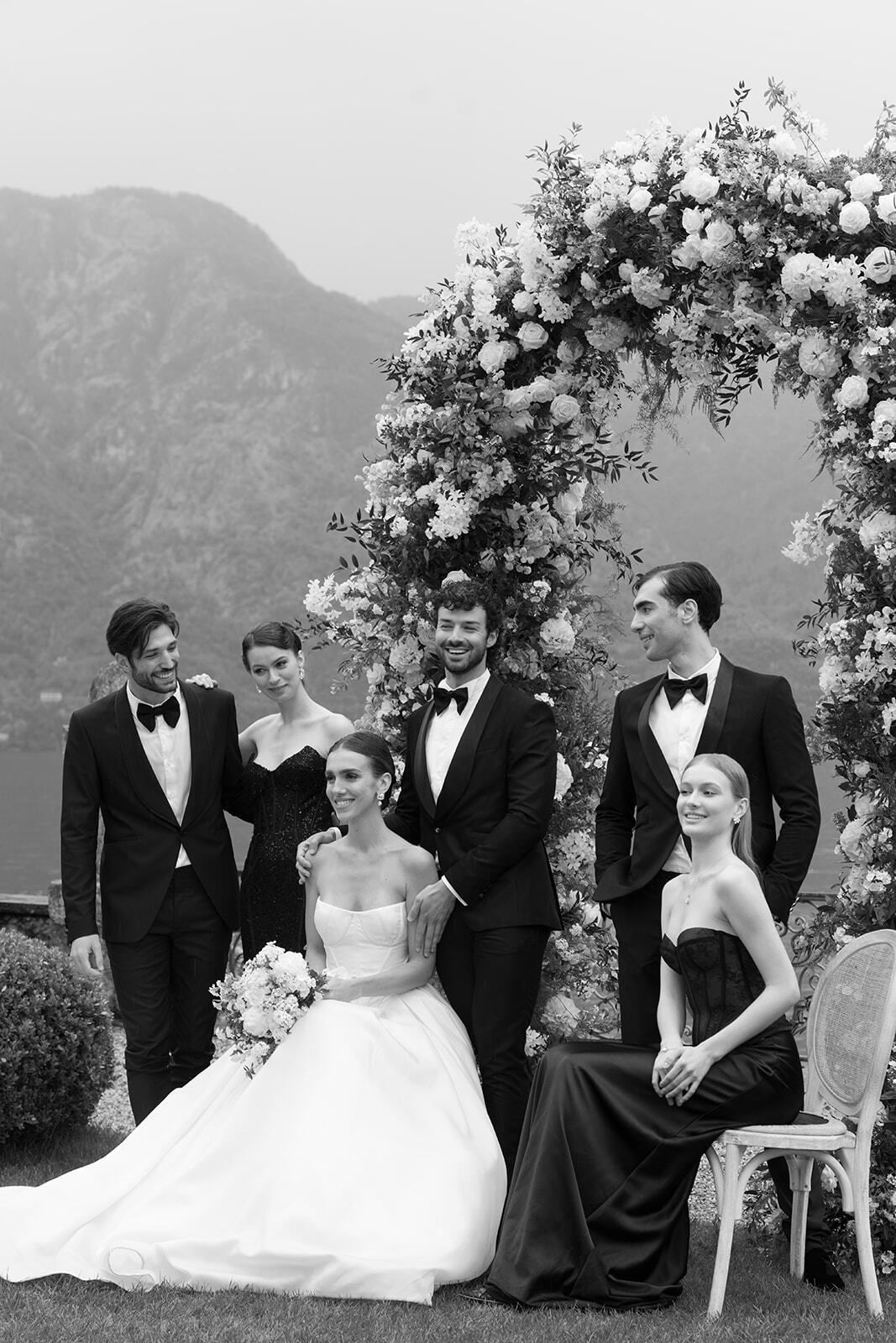 Schwarz-Weiß-Foto der Hochzeitsgesellschaft am Blumenbogen