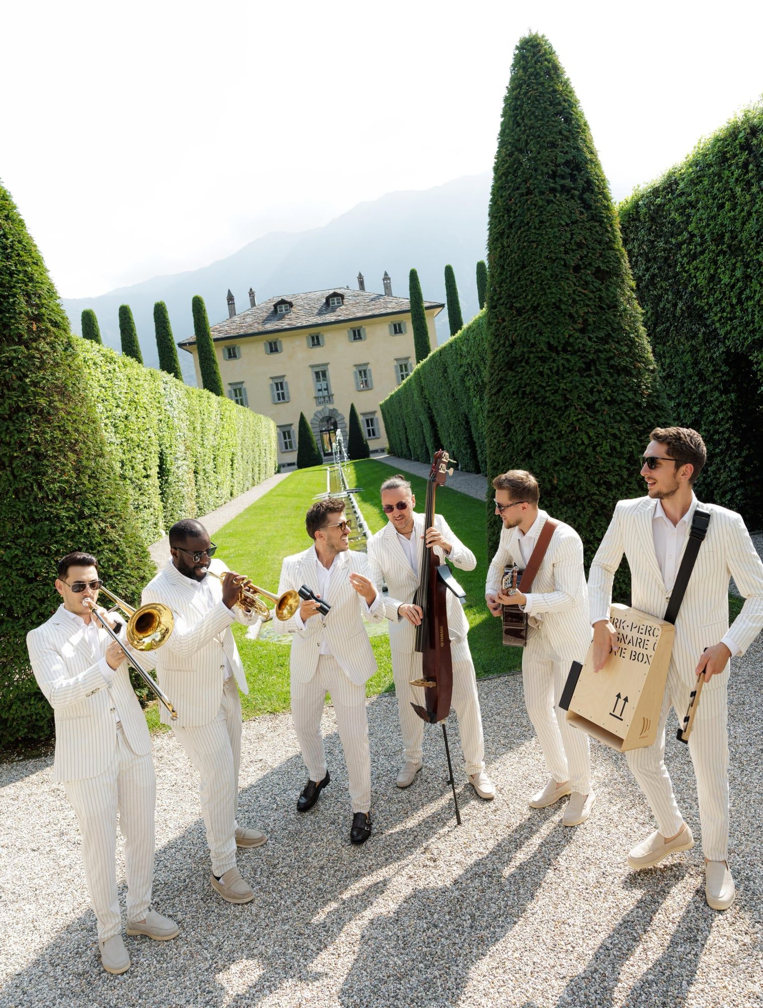 Musicians in white suits walking down the cypress avenue at Villa Balbiano