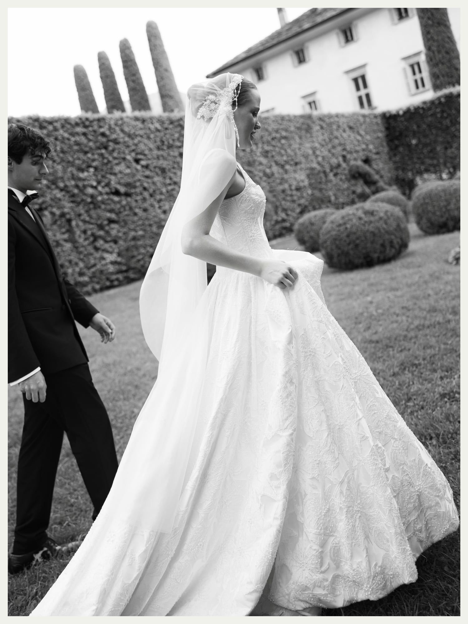 Black and white photo of a bride with a long veil walking through the garden at Villa Balbiano