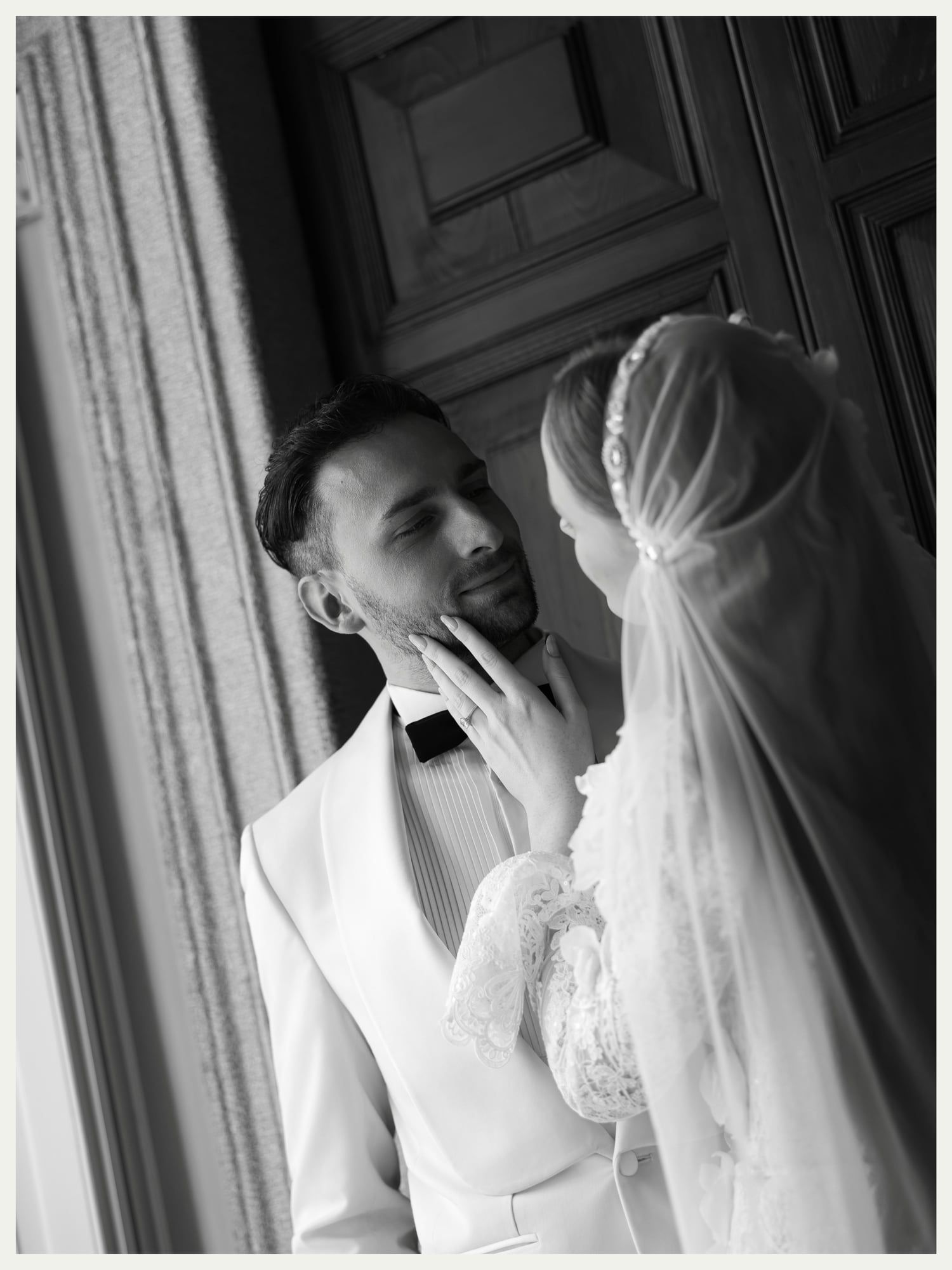 Black and white portrait of a groom touching the bride's face in a villa doorway