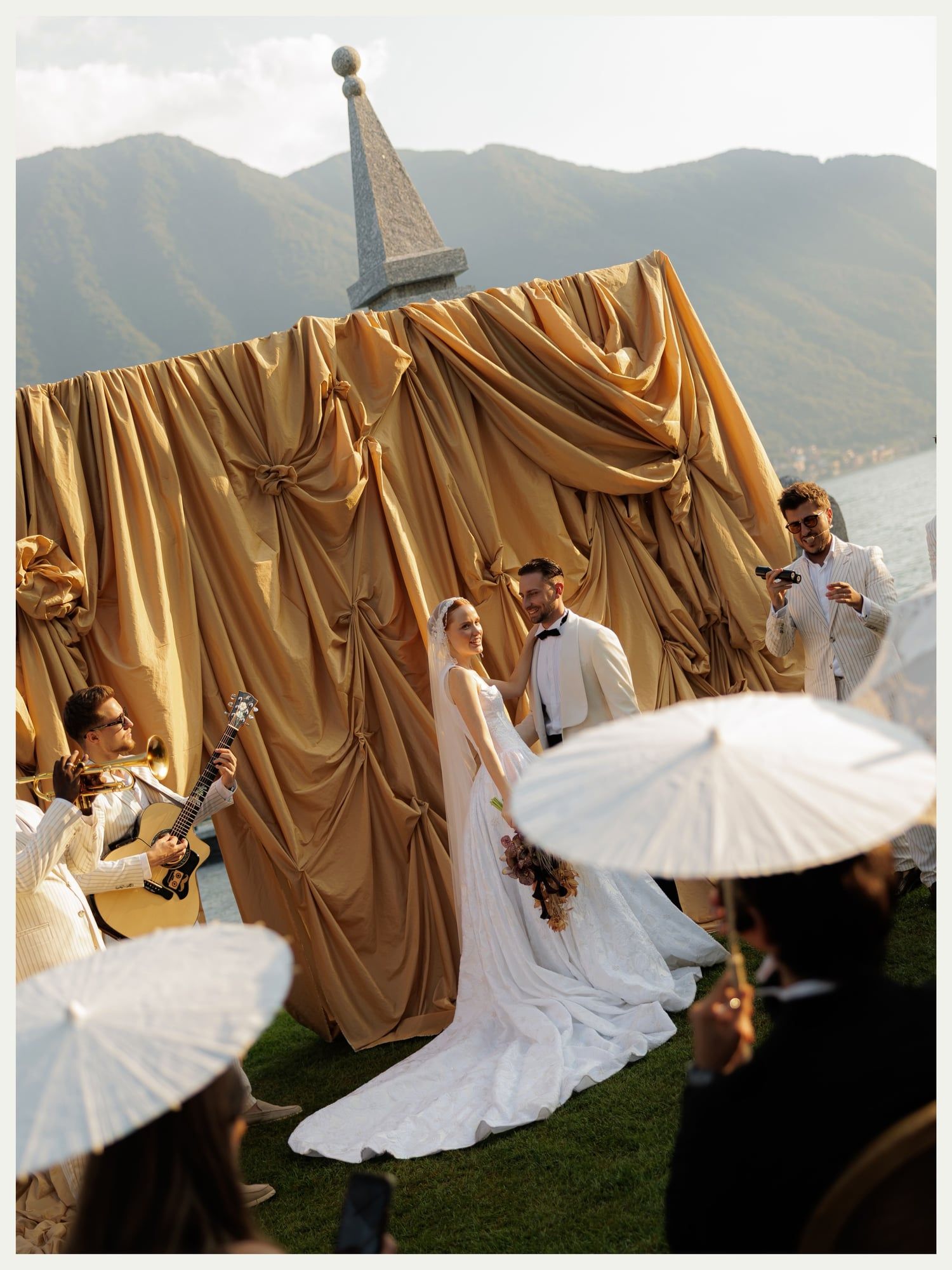 Couple at a gold-draped ceremony with guests holding white parasols, Lake Como