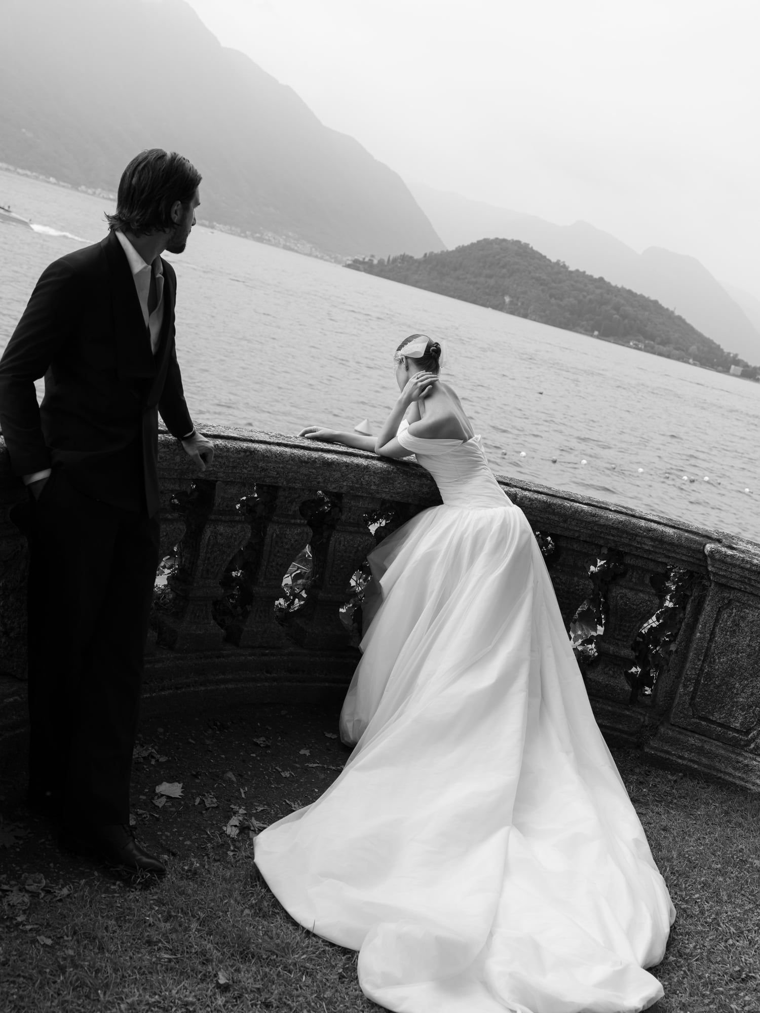 Black and white photo of a bride leaning on a stone balustrade above Lake Como