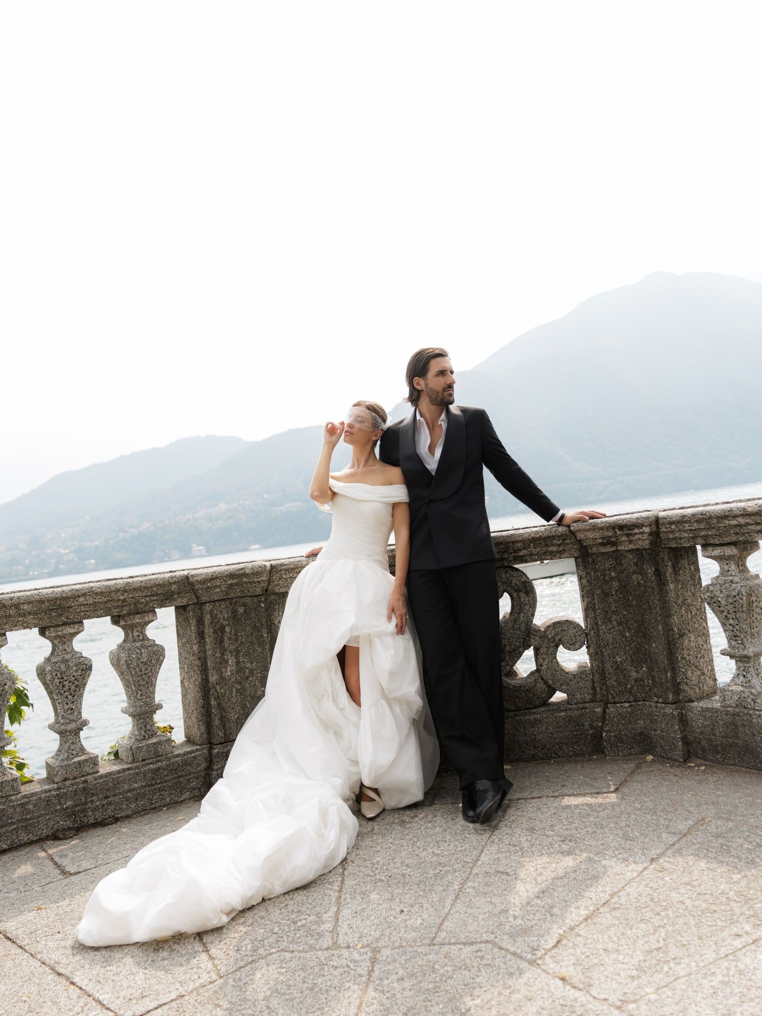 Bride and groom on a stone balustrade above Lake Como