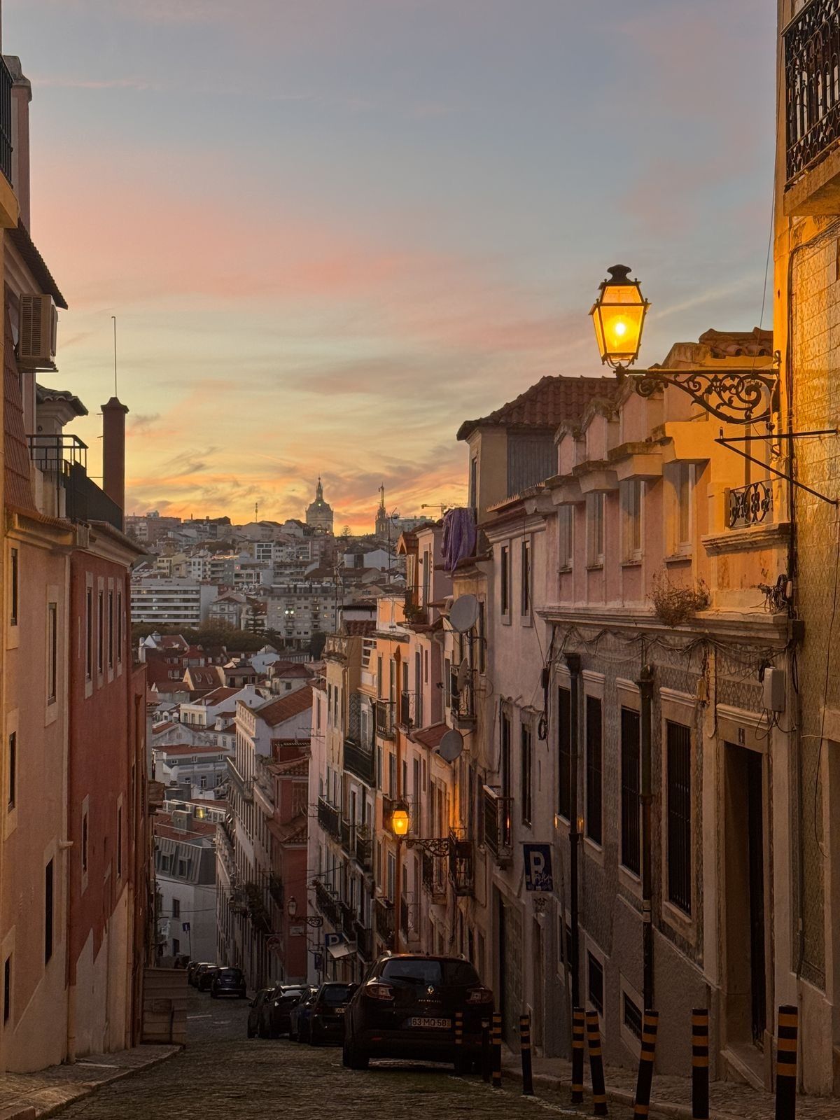 Straße in Lissabon bei Sonnenuntergang mit leuchtender Laterne und der Stadt darunter