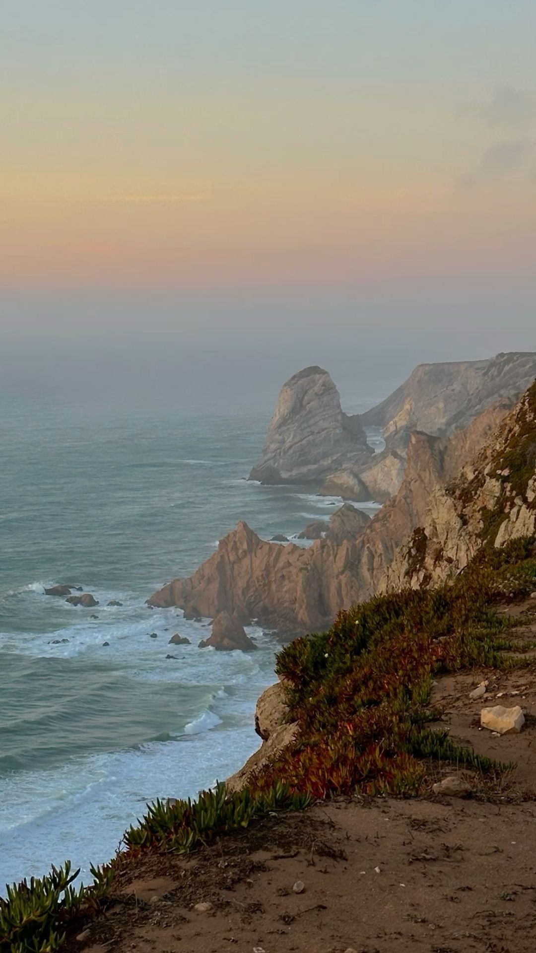 Felsige portugiesische Küste bei Sonnenuntergang mit Felsnadeln in der Ferne