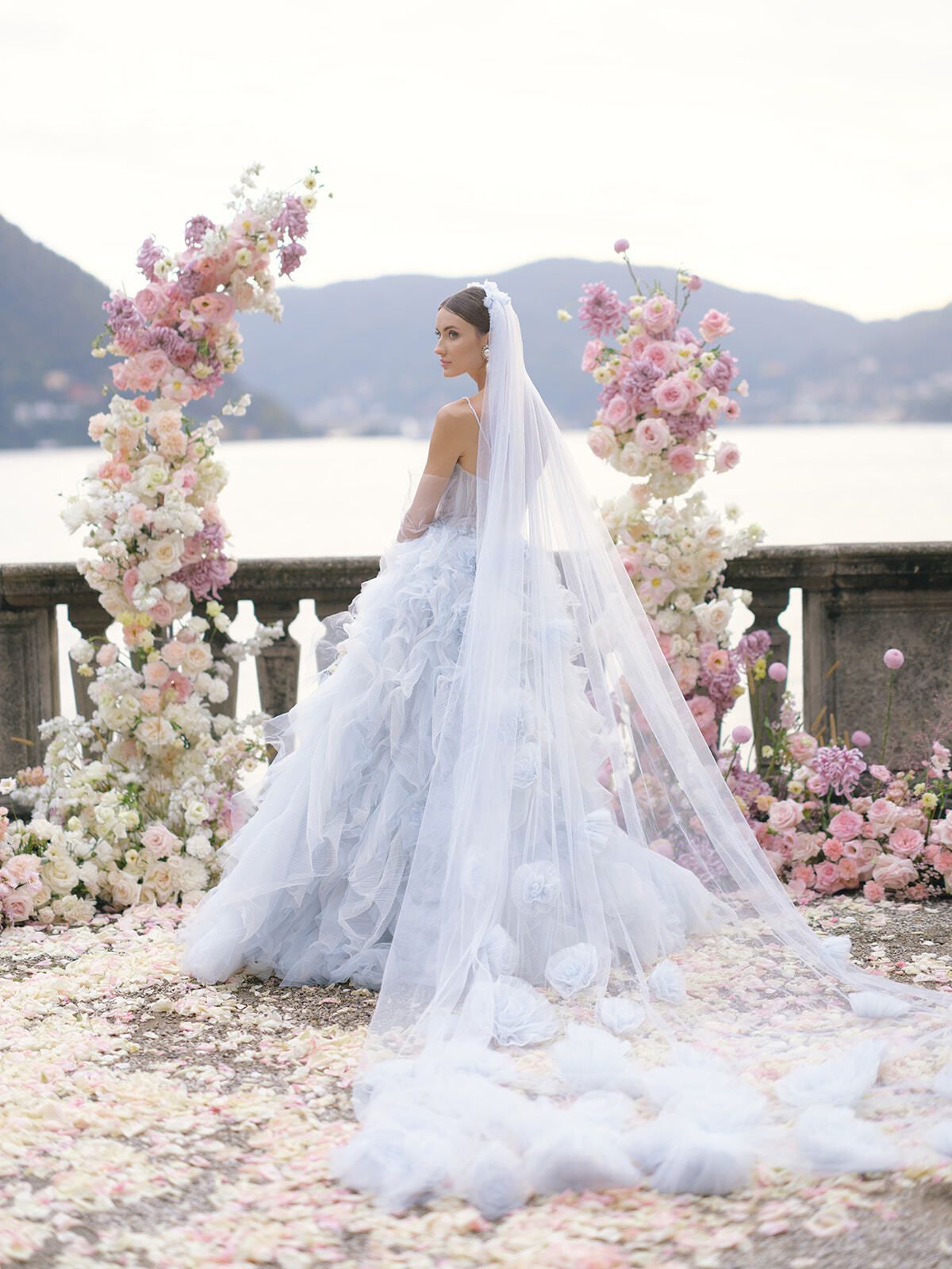 Novia con vestido de tul azul bajo un arco floral rosa, lago de Como