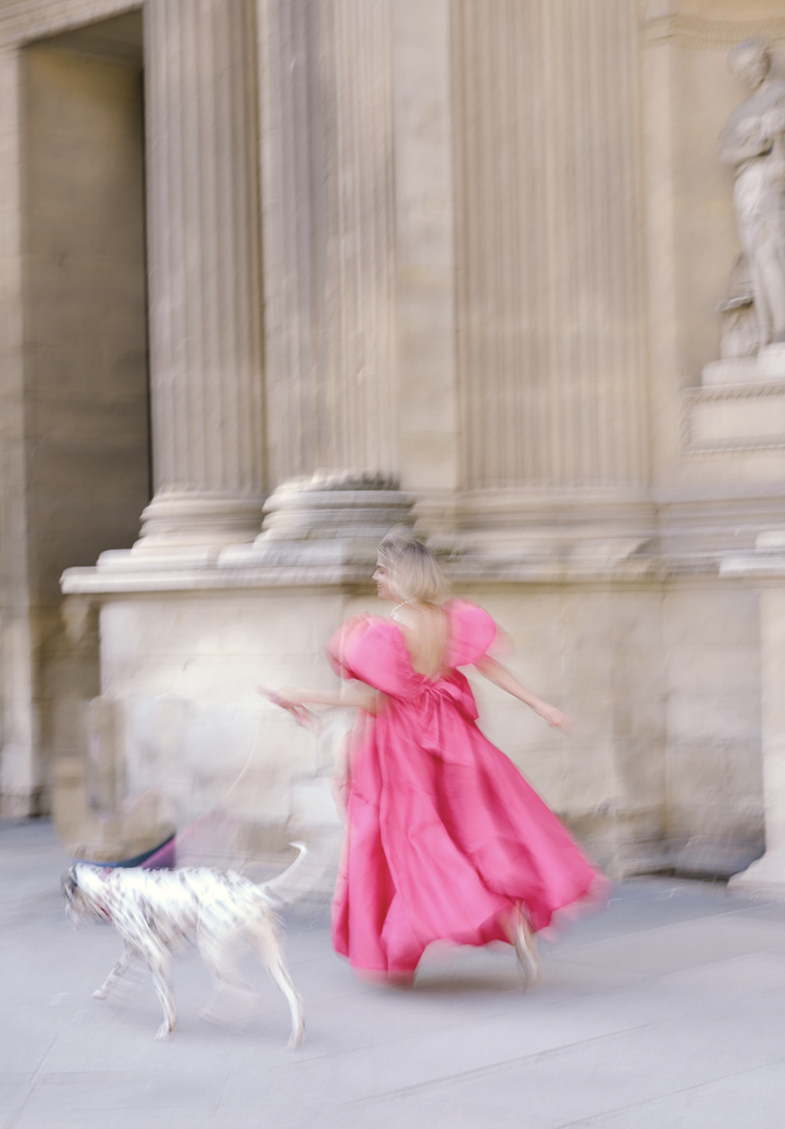 Mujer con vestido rosa corriendo con un dálmata por los soportales del Louvre