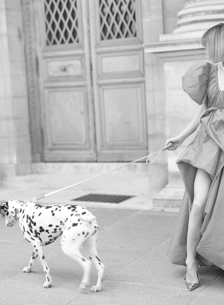 Foto en blanco y negro de una mujer paseando a un dálmata ante una puerta de París