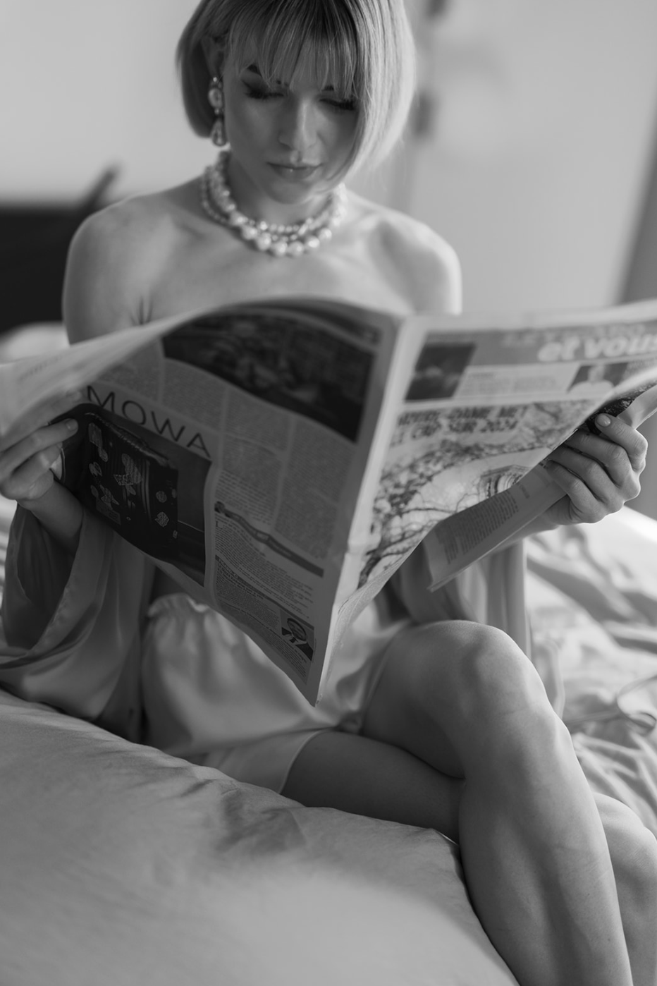 Foto en blanco y negro de una mujer con perlas leyendo el periódico