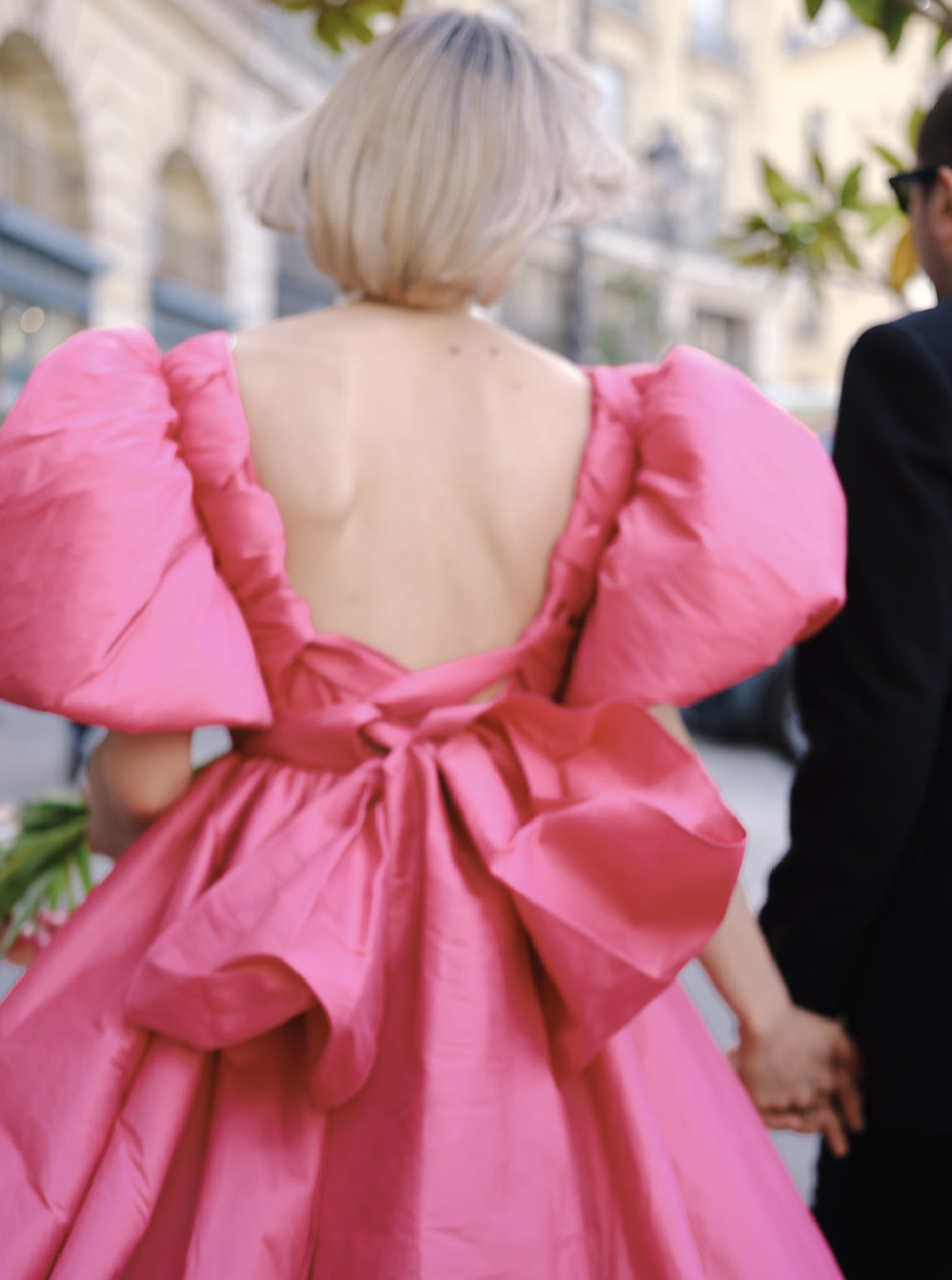 Espalda de una mujer con vestido rosa de mangas abullonadas caminando con su pareja