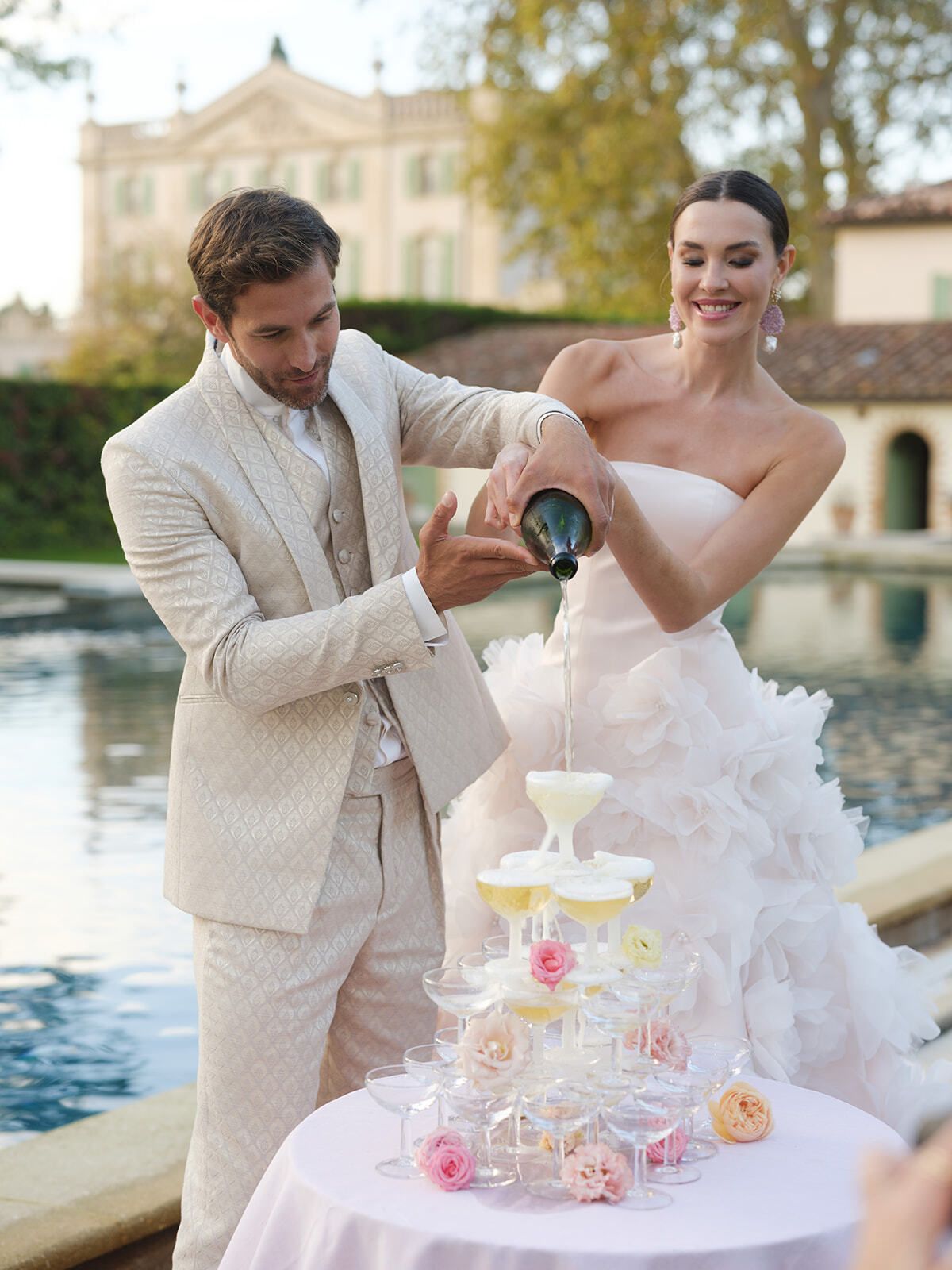 Sposo che versa champagne alla sposa a bordo piscina