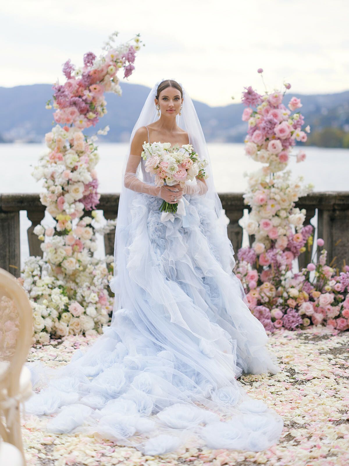 Novia de tul azul bajo un arco floral rosa junto al lago de Como