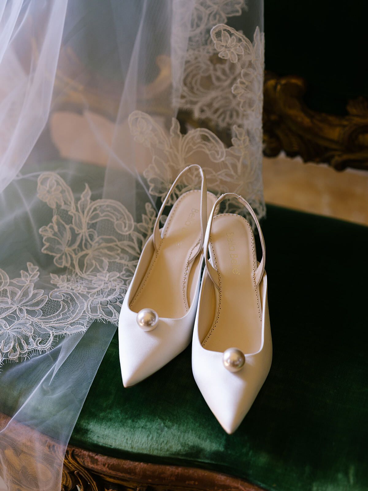 Scarpe da sposa avorio accanto a un velo di pizzo su velluto verde