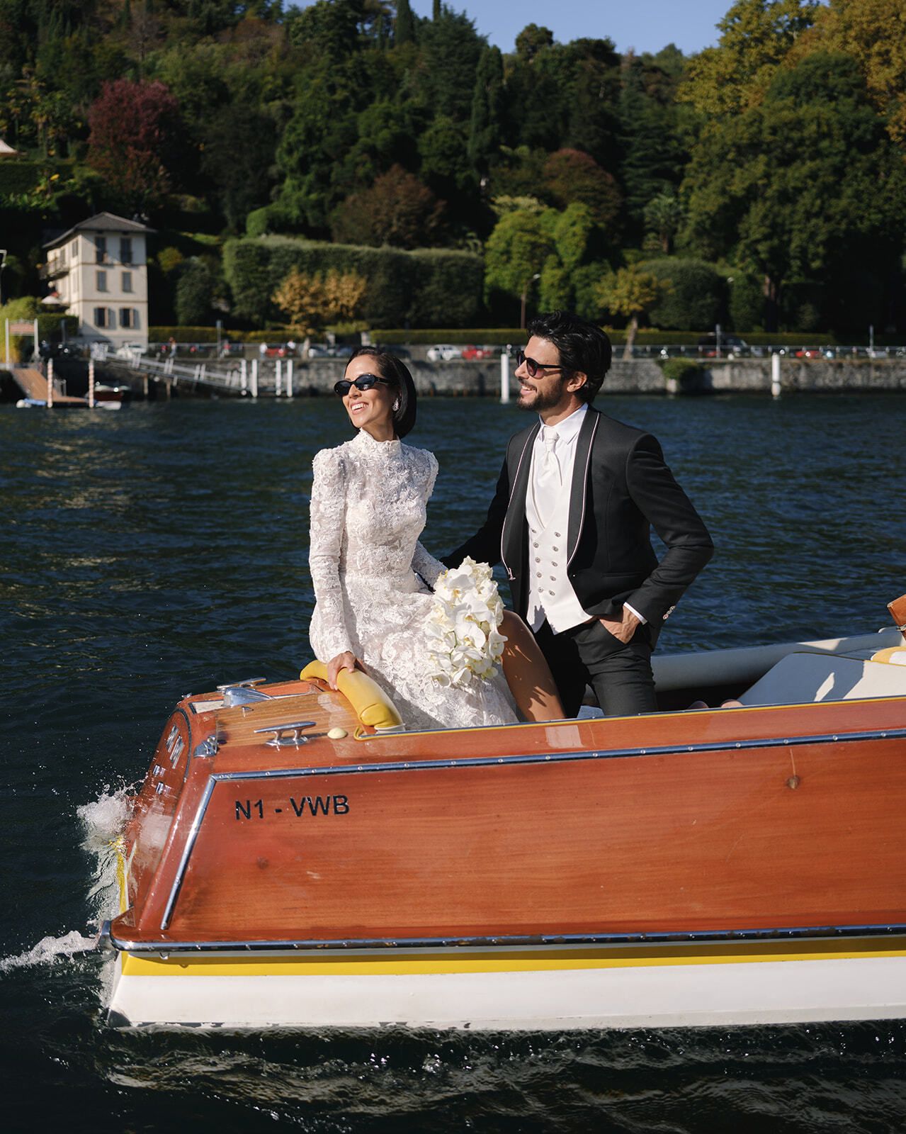 Braut in Spitze und Bräutigam stehen auf einem schnellen Holzboot