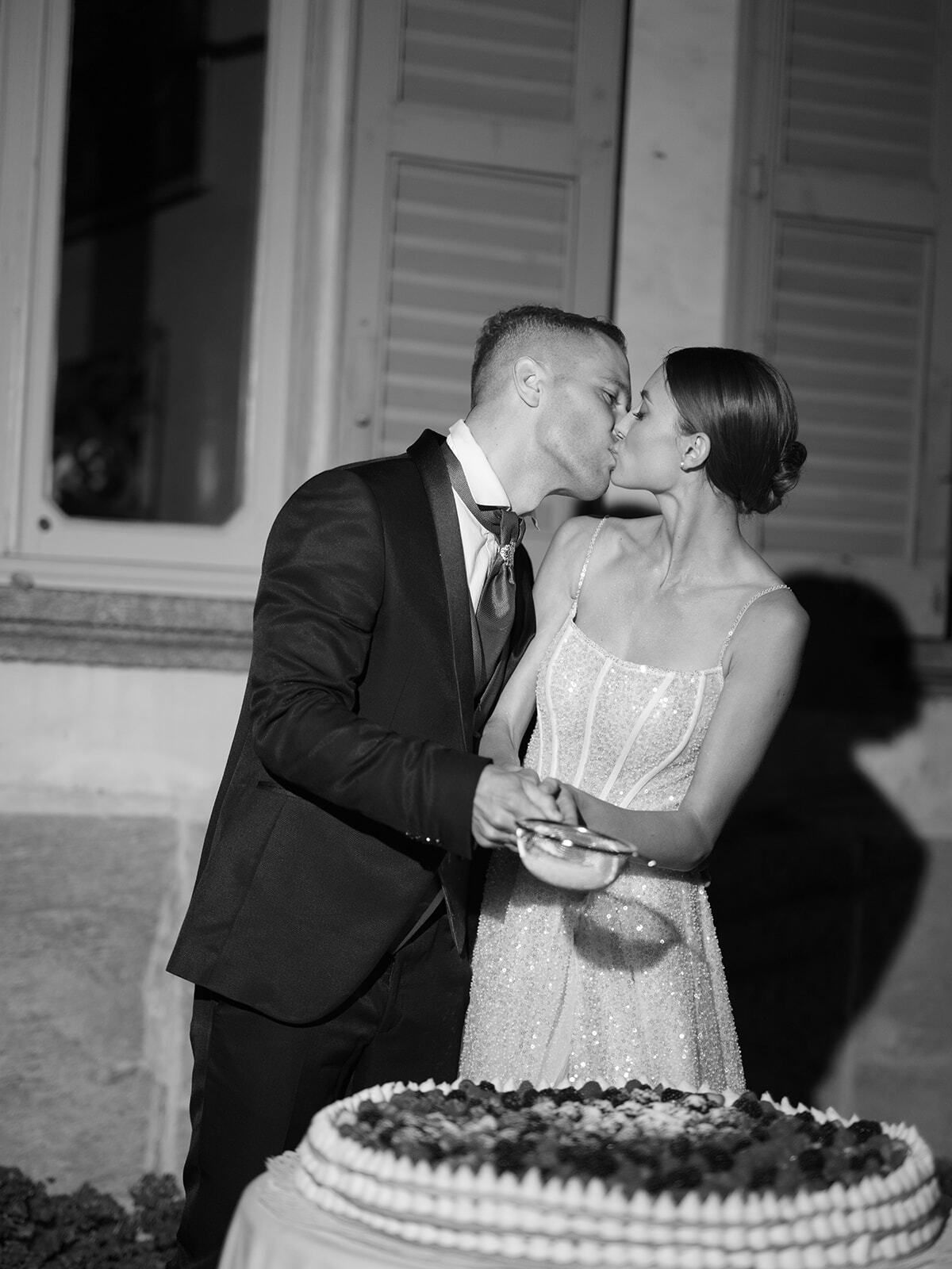 Foto en blanco y negro de la pareja besándose sobre su tarta de boda