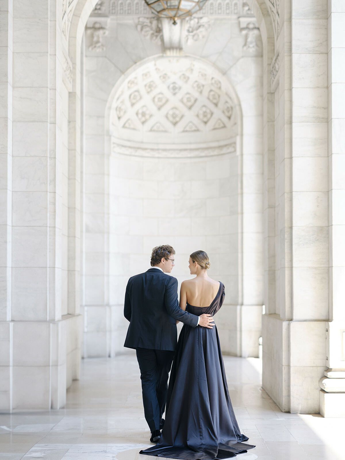 Pareja con vestido y traje azul marino en un salón de mármol blanco