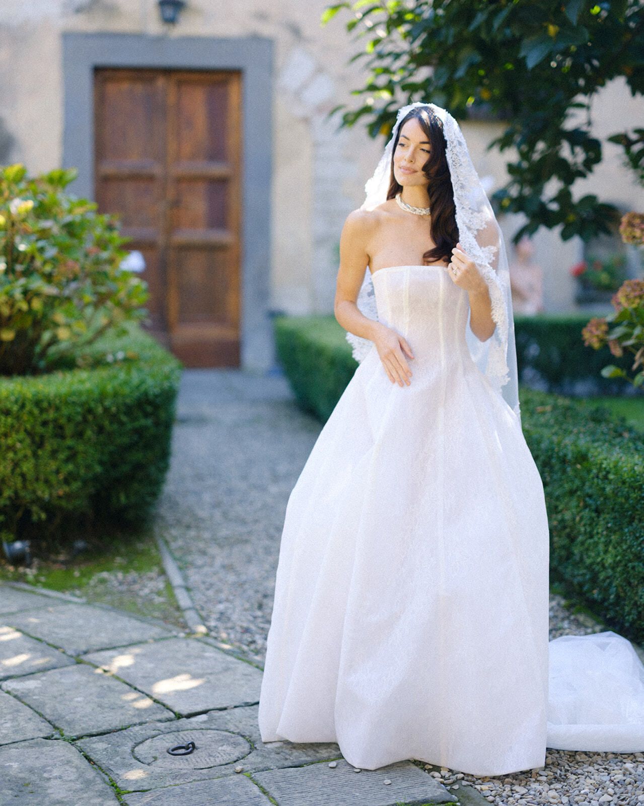 Novia con vestido palabra de honor y velo de encaje en el patio de la villa