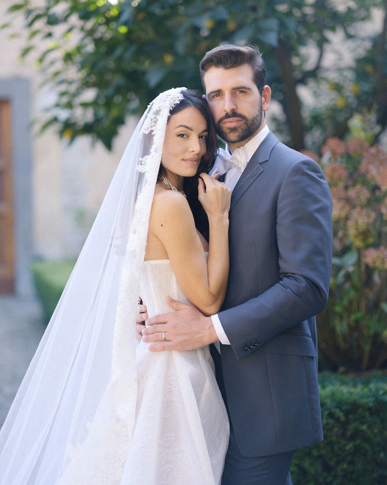 Novio abrazando a la novia con velo en un jardín toscano