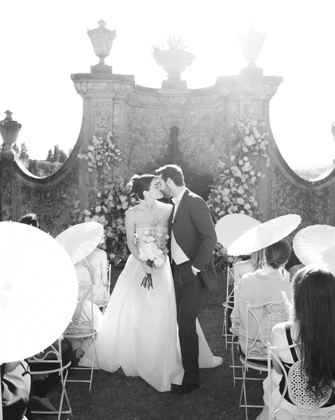 Foto en blanco y negro del beso de la ceremonia entre sombrillas
