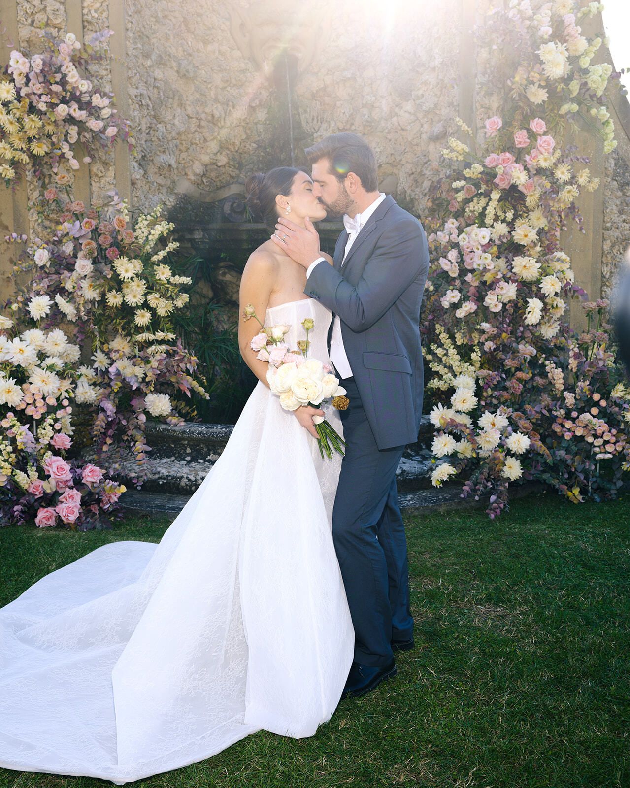 Novios besándose ante una gruta cubierta de flores en la Toscana