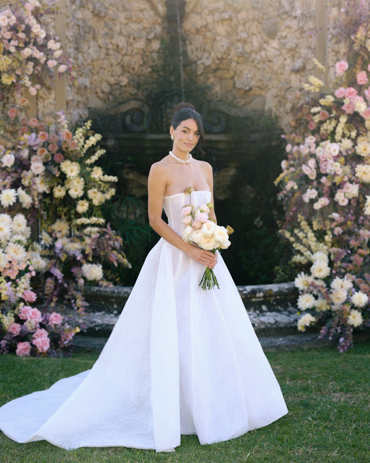 Novia con un ramo ante la gruta cubierta de flores