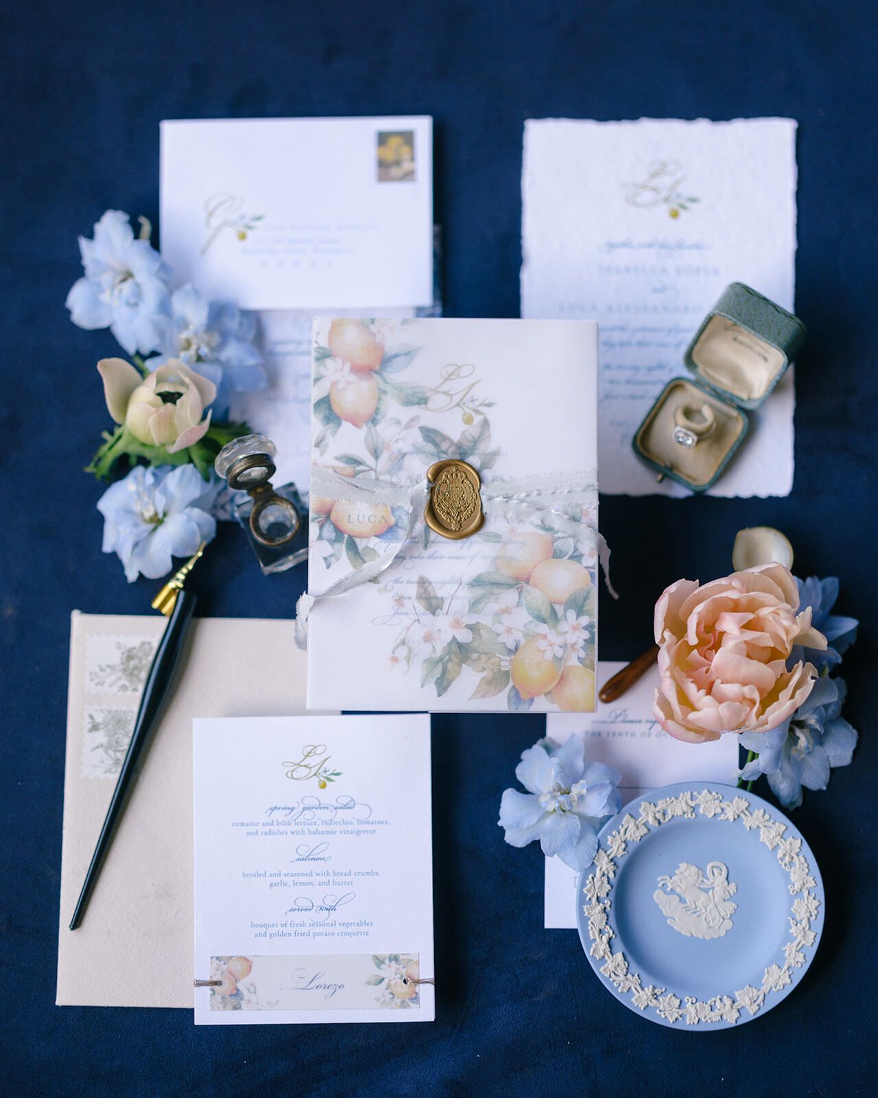 Papelería de boda con flores azules y un plato Wedgwood sobre terciopelo azul marino