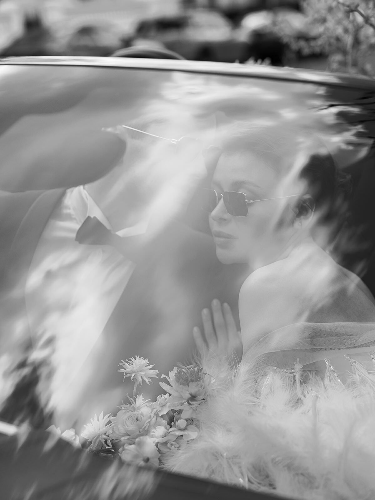 Schwarz-Weiß-Foto einer Braut, die sich in einem Autofenster spiegelt