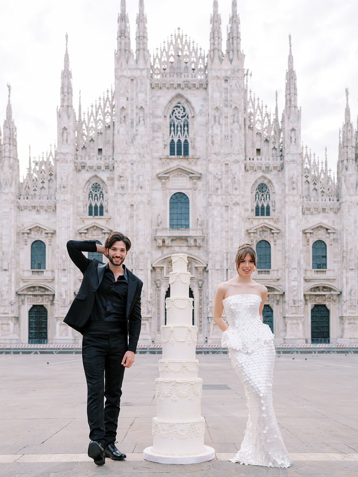 Couple posing with a tall white cake before Milan Cathedral