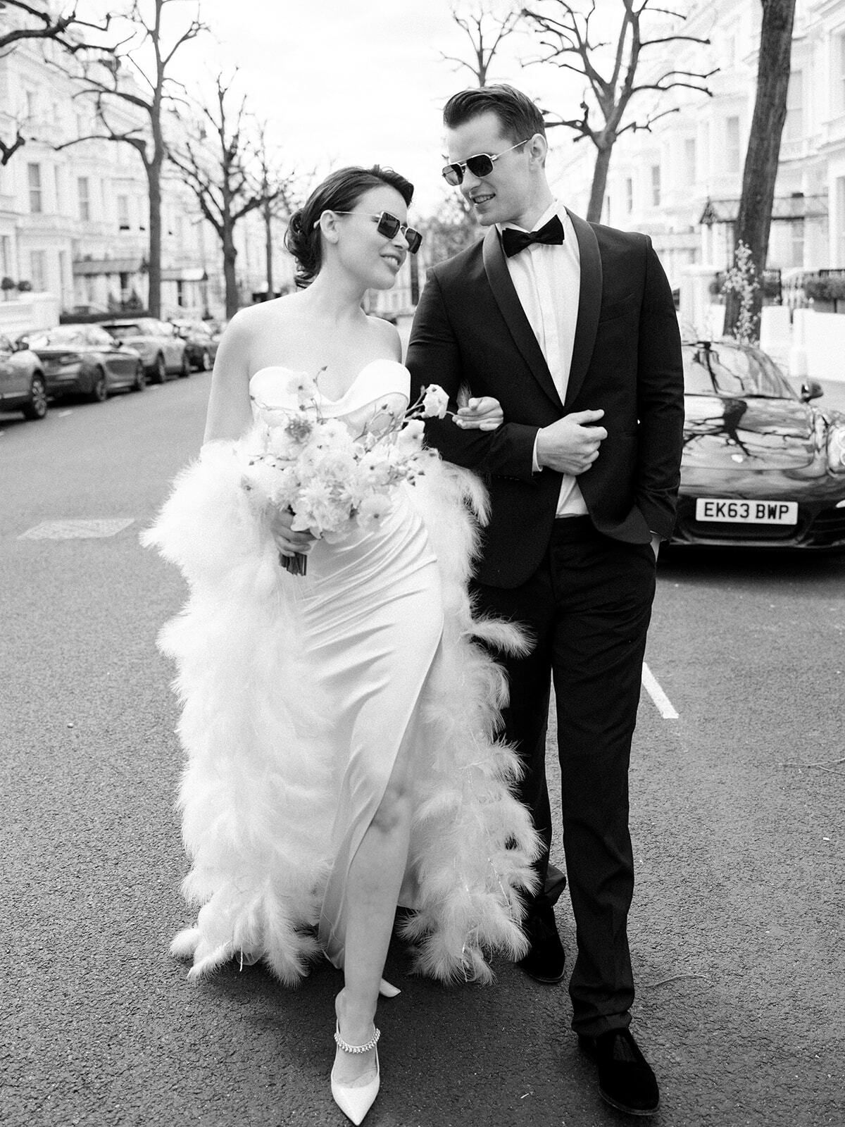 Schwarz-Weiß-Foto einer Braut im Federkleid mit dem Bräutigam in einer Londoner Straße