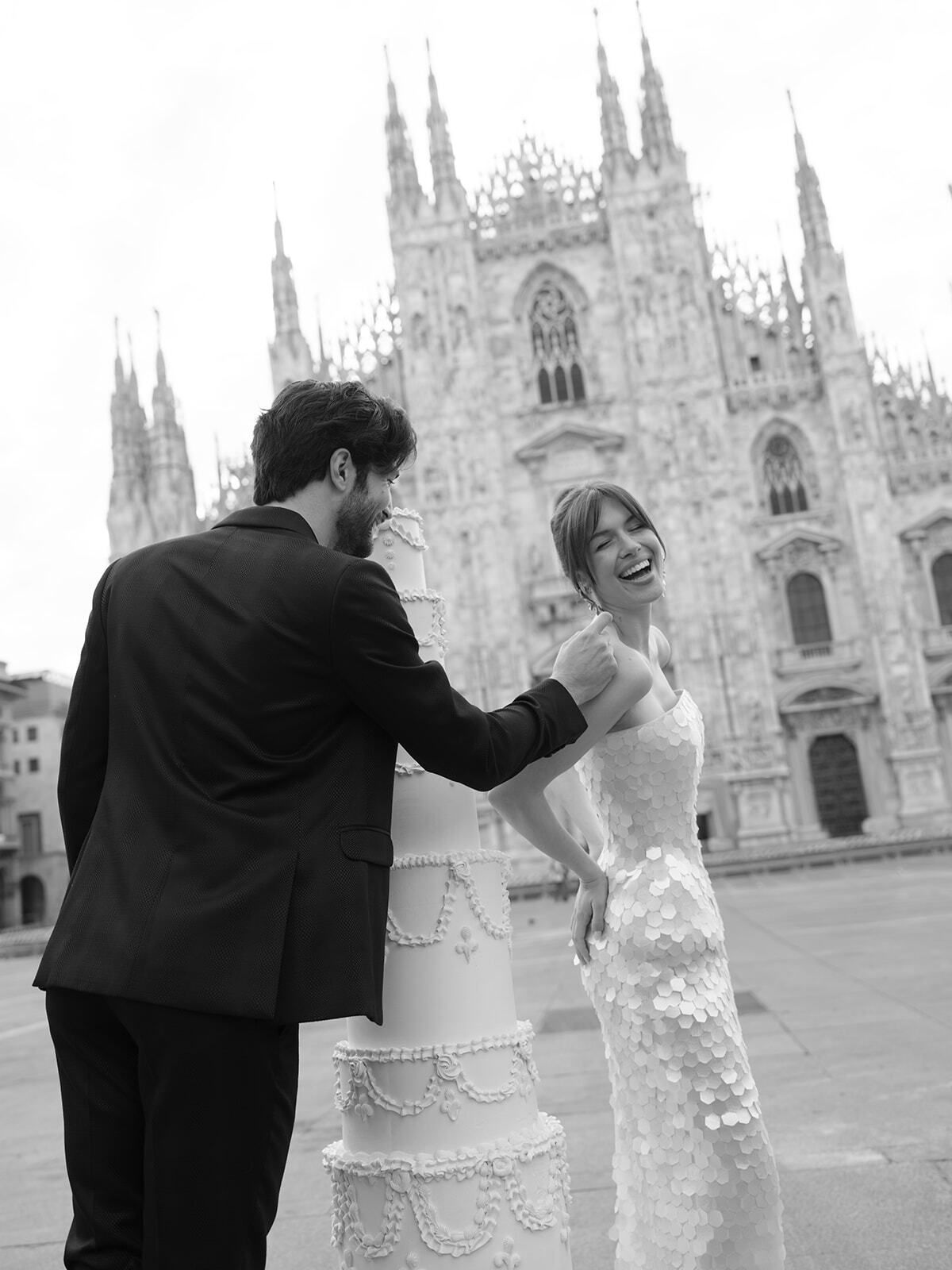 Black-and-white photo of a couple with a cake before Milan Cathedral