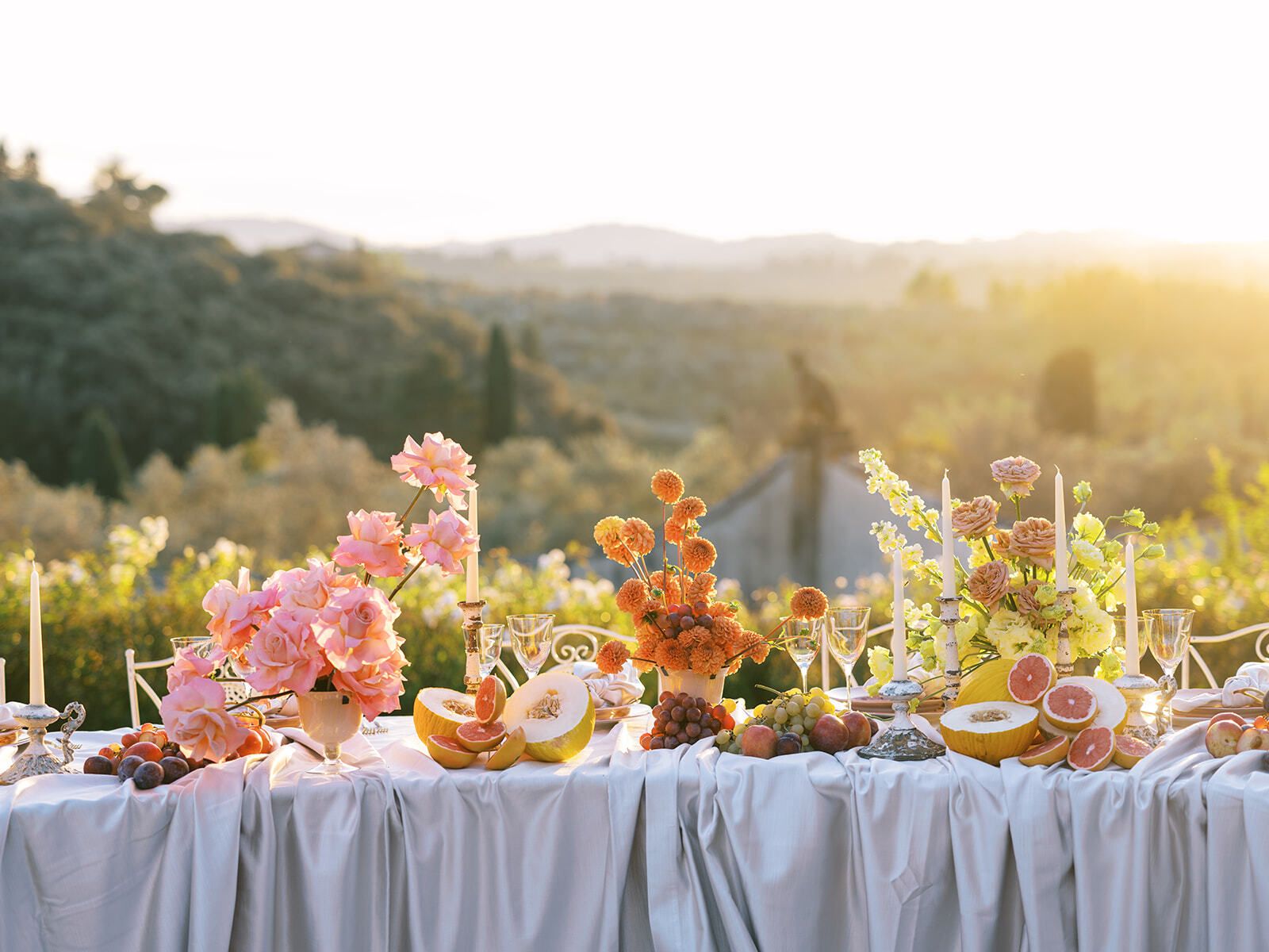 Mesa larga de banquete con fruta y flores con vistas a las colinas toscanas