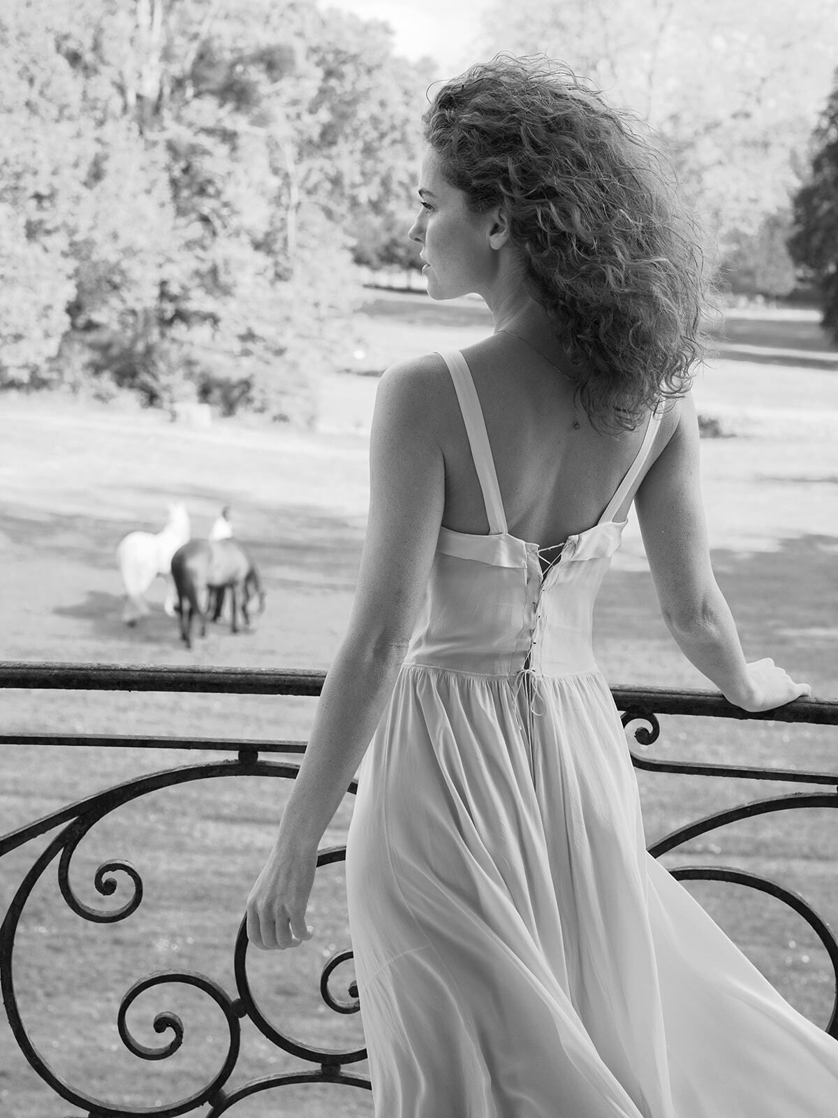 Foto en blanco y negro de una novia en el balcón de un château con caballos abajo