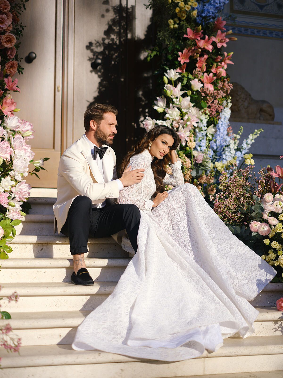 Novios sentados en la escalinata flanqueada de flores de Villa Clara