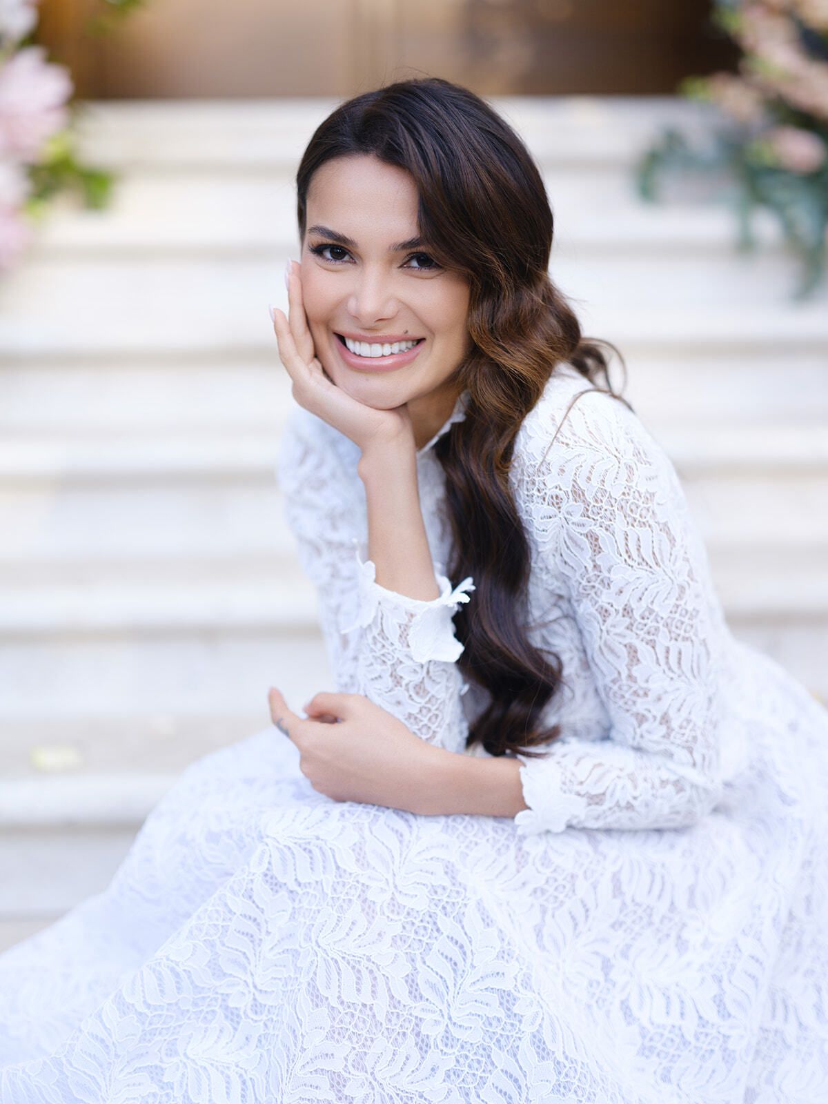Novia sonriente con vestido de encaje sentada en unos escalones de mármol