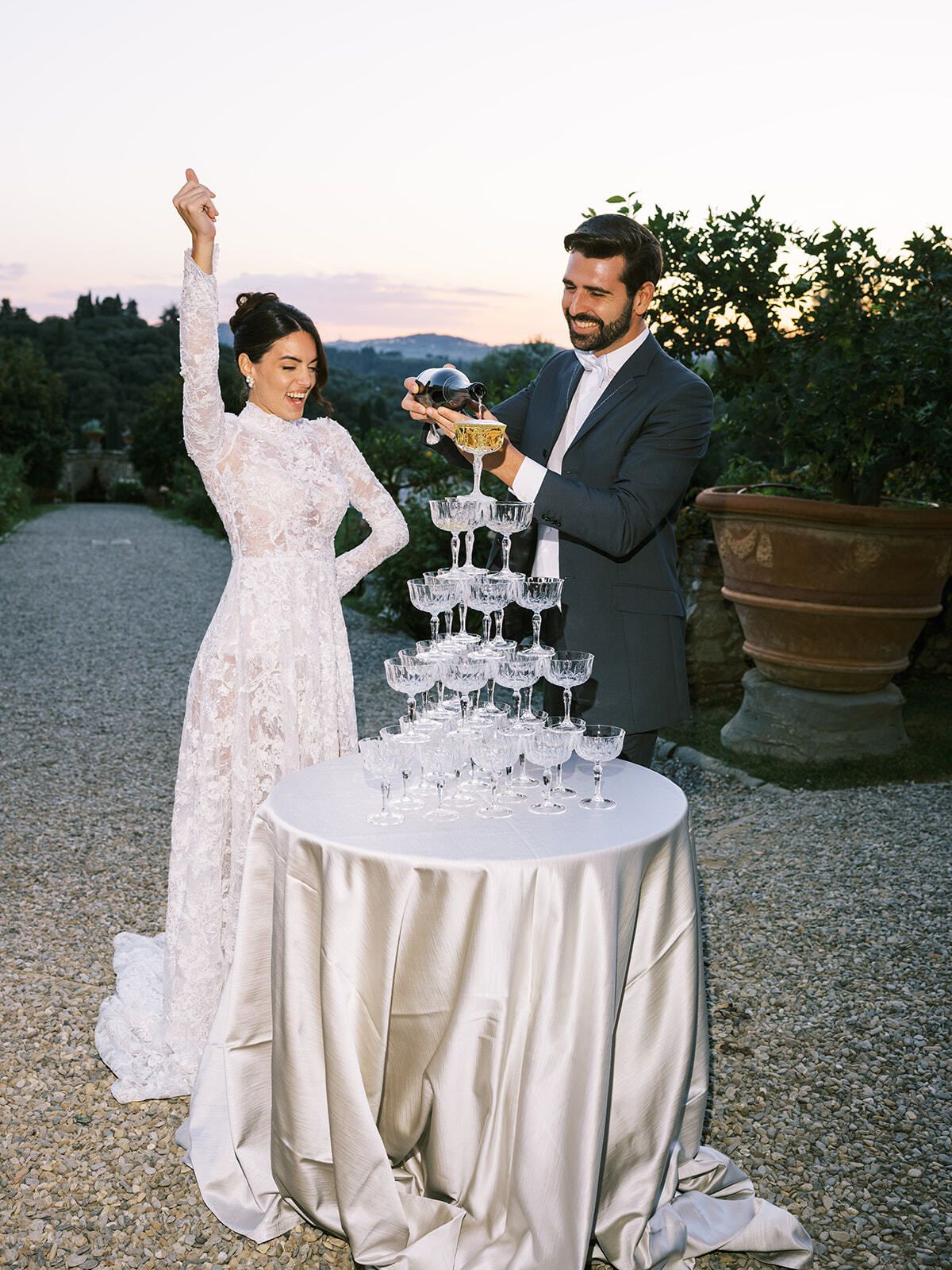 Novia celebrando mientras el novio sirve una torre de champán, Toscana