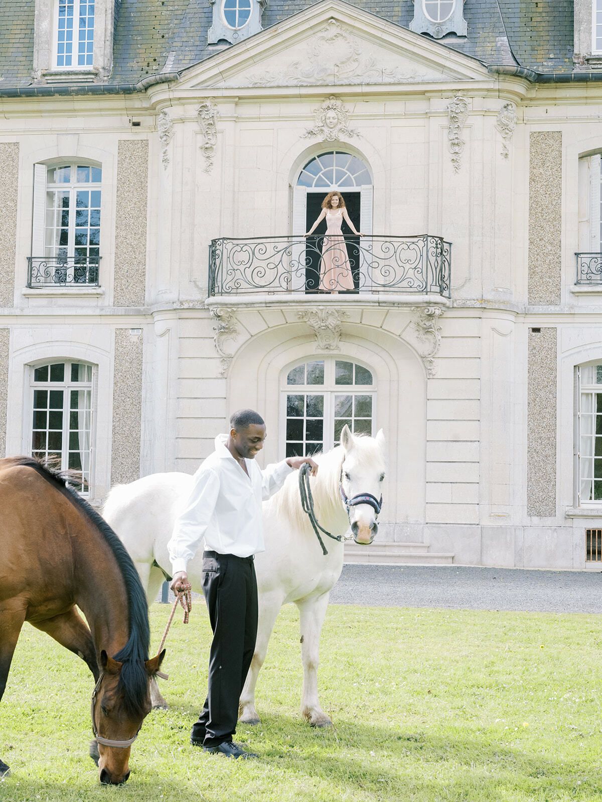Novio con caballos en el césped de un château de Normandía, la novia en el balcón