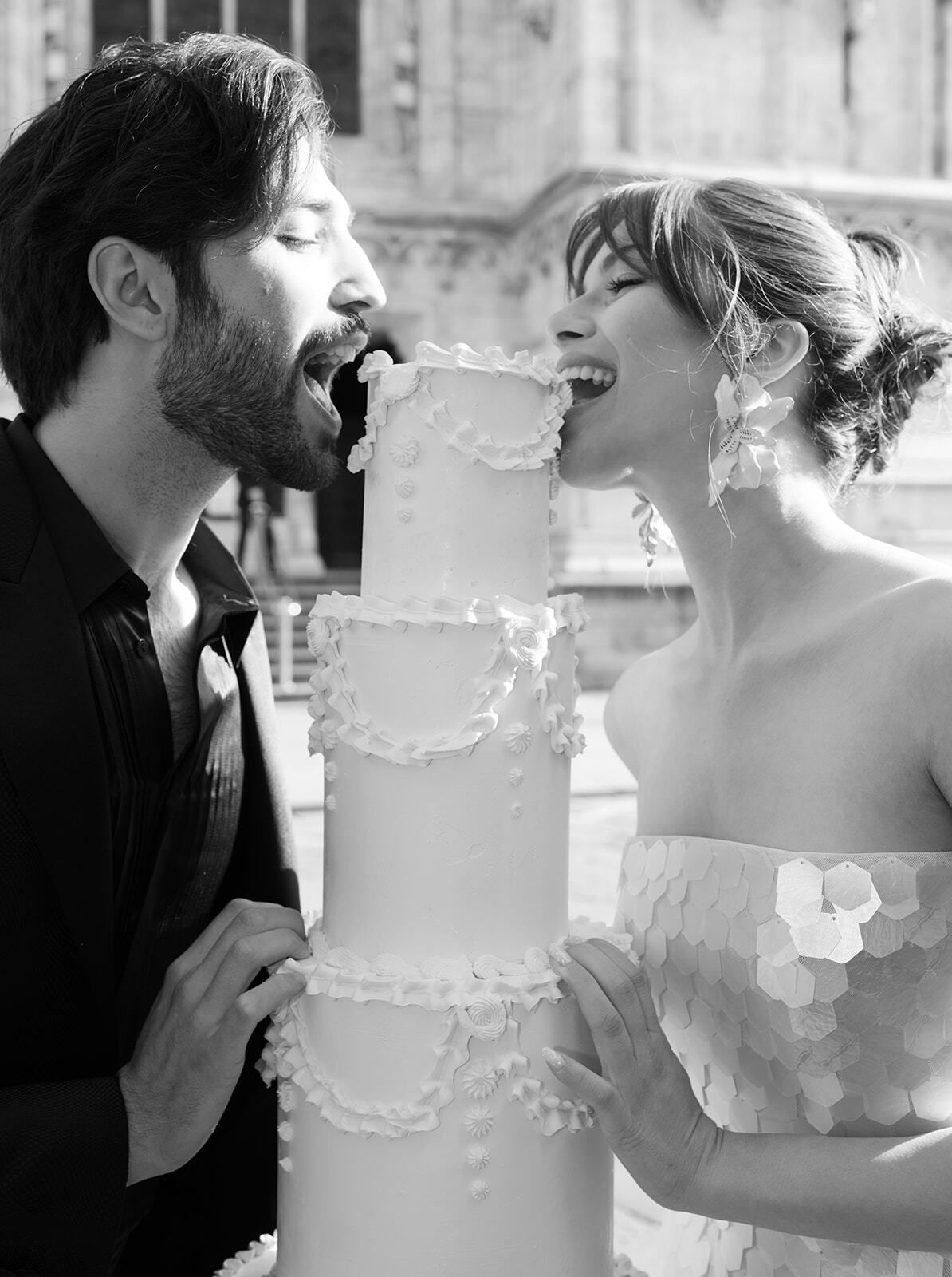 Black-and-white photo of a couple tasting a tiered wedding cake