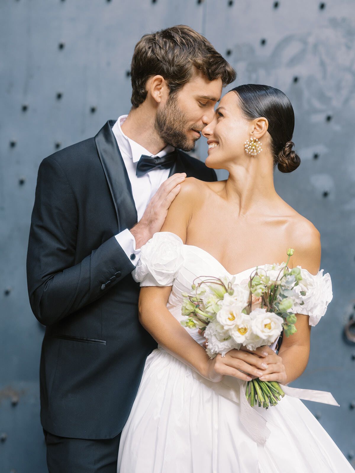 Novios ante una puerta azul con un ramo blanco
