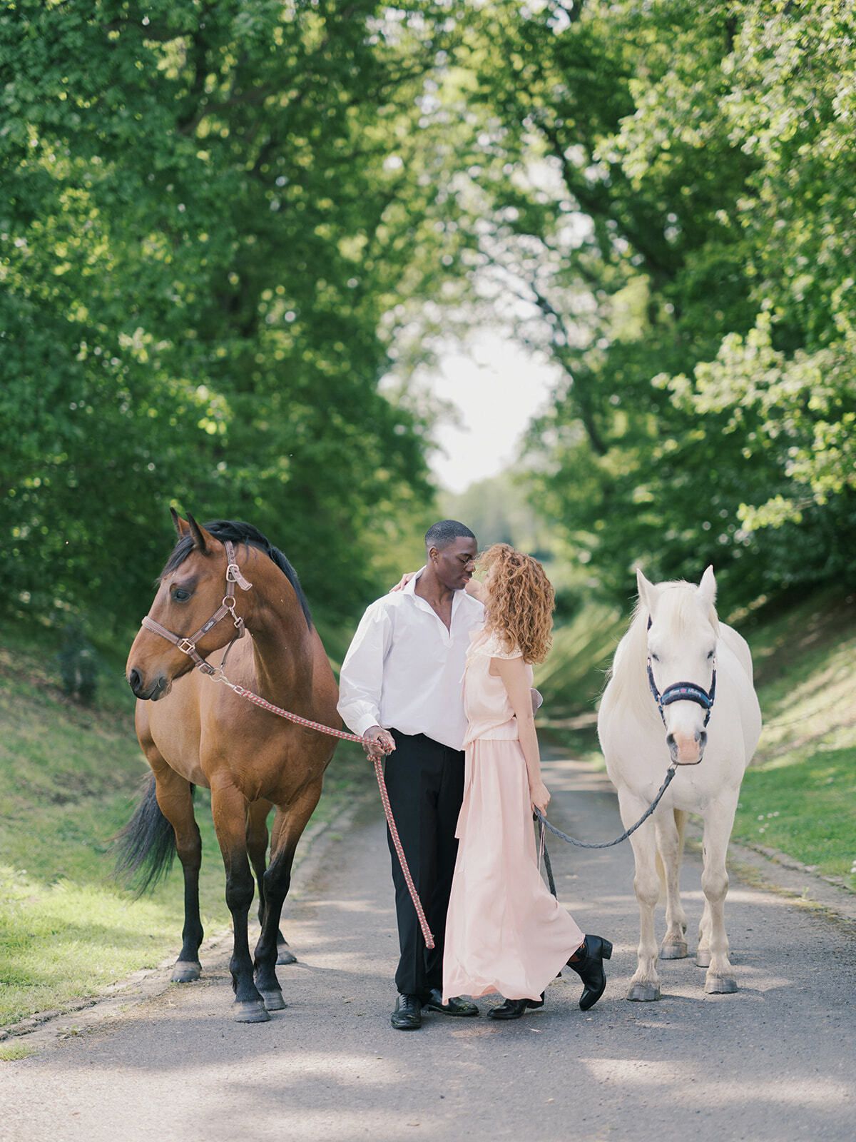 Pareja paseando dos caballos por un camino arbolado en Normandía