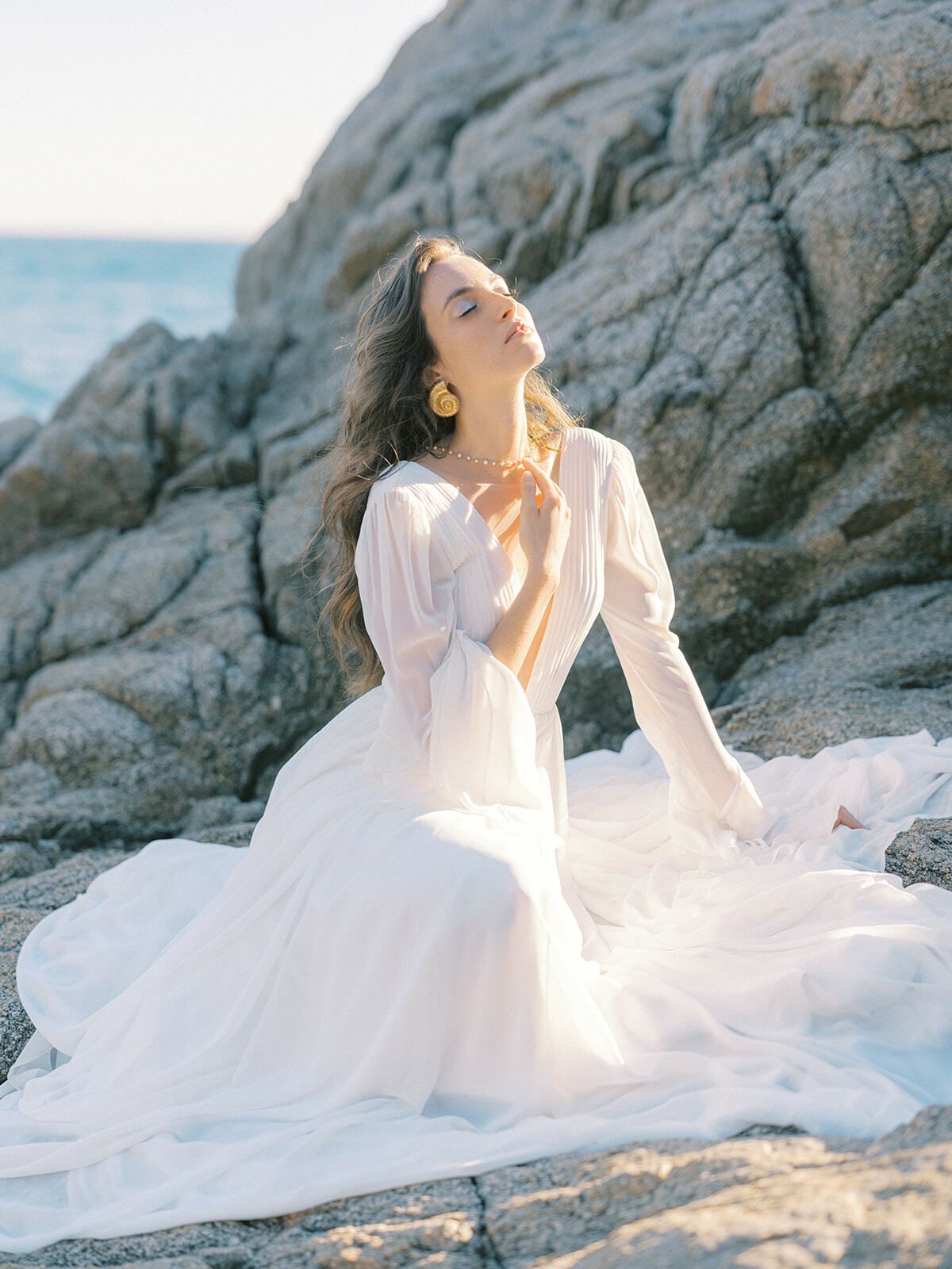 Braut in einem fließenden weißen Kleid auf Felsen am Meer