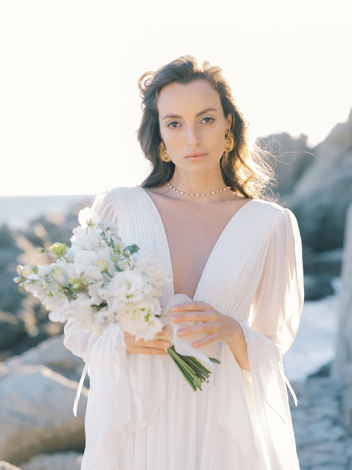 Braut in einem Boho-Kleid mit tiefem Ausschnitt auf den Felsen der Costa Brava