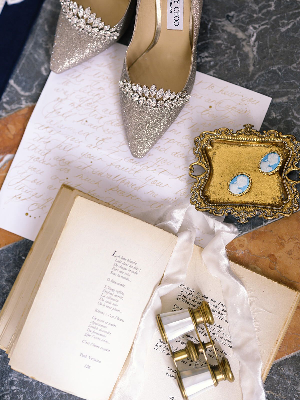 Zapatos de novia con pedrería junto a unos gemelos de teatro y un libro abierto